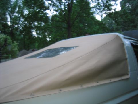 1996 Ford Bronco - Low-angle close-up of a tan vinyl soft top stretched over a vehicle's rear roofline, with a small diamond-shaped clear plastic window and a…