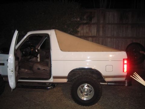 1996 Ford Bronco - Night shot of the driver's side of a white full-size Ford Bronco with a tan soft top and the door open, revealing the tan interior, bucket…
