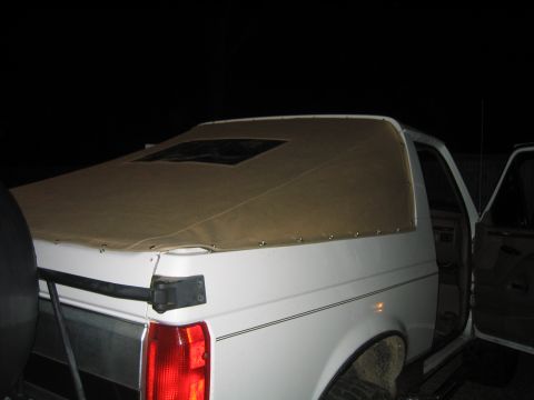 1996 Ford Bronco - Night flash photo of the rear three-quarter of a white full-size SUV with a tan vinyl soft top snapped over the cargo area in place of the…