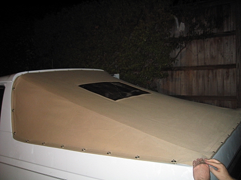 1996 Ford Bronco - Night flash shot looking down the tan vinyl soft top fitted over the rear section of a white SUV, showing the small rectangular clear windo…