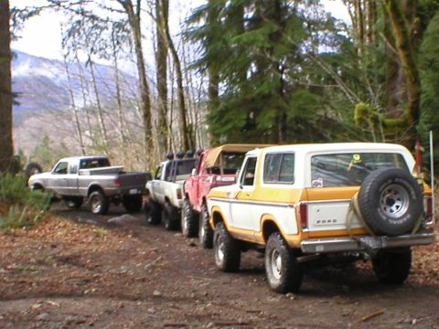 1978 Ford Bronco - Several off-road vehicles, including a 1978 Ford Bronco, are parked on a dirt trail surrounded by trees.