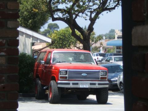 1988 Ford Bronco - A red Ford Bronco is parked in front of a building, with other vehicles visible in the background.