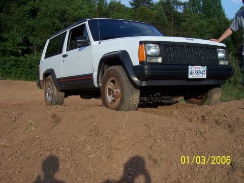 1995 Jeep Cherokee - A white 1995 Jeep Cherokee is partially submerged in dirt, with a person's arm resting on the hood.