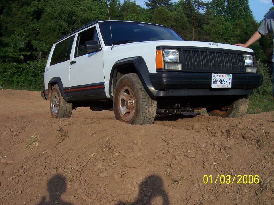 White 1995 Jeep Cherokee with a black grille and fender flares, stuck in dirt