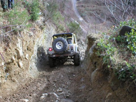 1978 Ford Bronco - A yellow jeep carefully maneuvers through a challenging off-road terrain with steep dirt banks on either side.