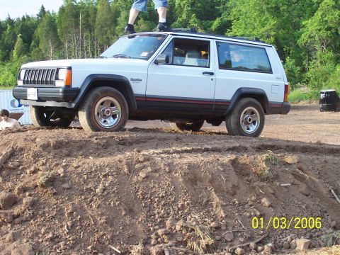 1995 Jeep Cherokee - A white 1995 Jeep Cherokee 3-door is positioned on a dirt mound, with a person standing on its roof.