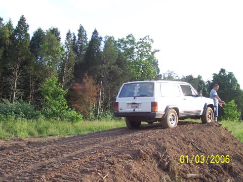 1995 Jeep Cherokee - White 1995 Jeep Cherokee sits on a dirt pile with a wooded area behind it.