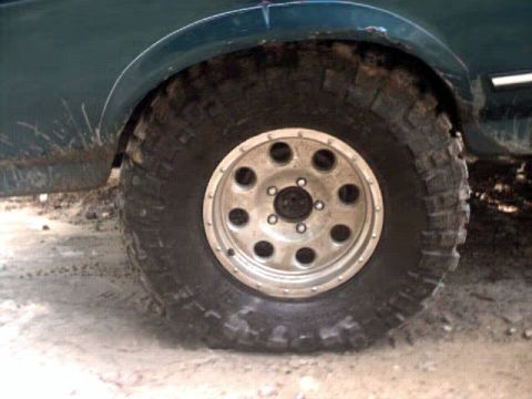 1996 Ford Bronco - Close-up of a muddy tire and fender on a dark green SUV, showing off-road modifications.