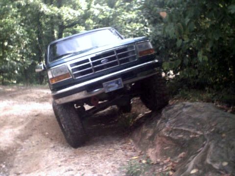 1996 Ford Bronco - Ford Bronco navigating a challenging off-road obstacle on a wooded trail.