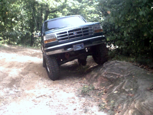 Green Ford Bronco climbing over a rock on a dirt trail