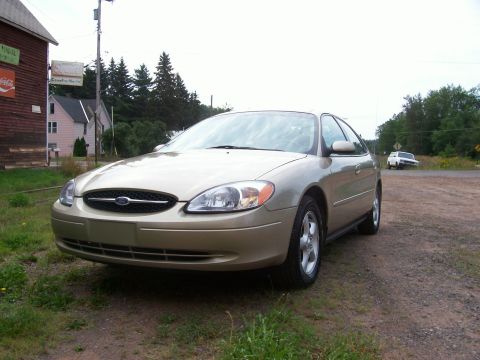 2000 Ford Taurus - A gold sedan is parked on a gravel road with a building and trees in the background.