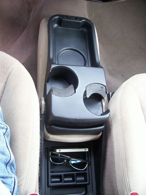 2000 Ford Taurus - The center console of a vehicle, cup holders and a storage area with sunglasses and a phone inside.