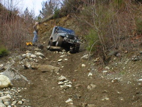 1978 Ford Bronco - A Jeep CJ-7 is shown attempting to traverse a difficult off-road course with steep inclines and loose terrain.