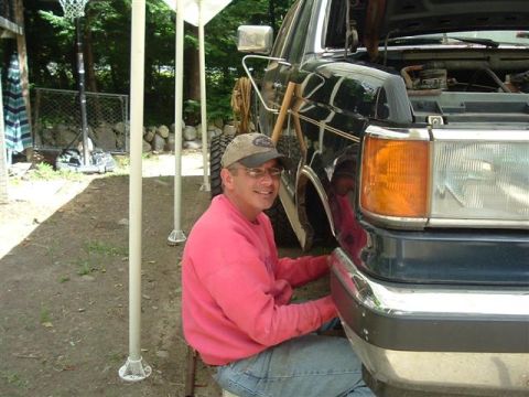 1991 Ford Bronco - Man works on the front bumper of a 1991 Ford Bronco with the hood open.