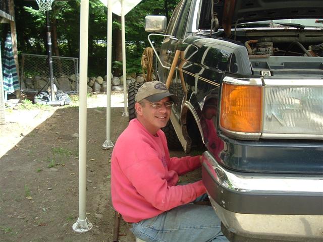 Man in pink sweatshirt and baseball cap working on the front bumper of a 1991 Ford Bronco