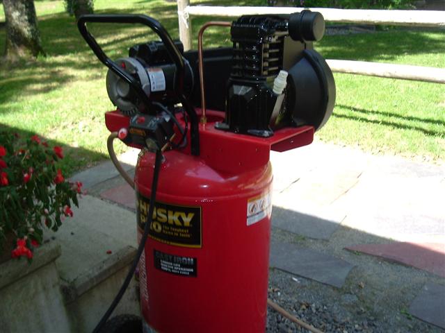 red Husky air compressor with black motor and tank, outside on paved area