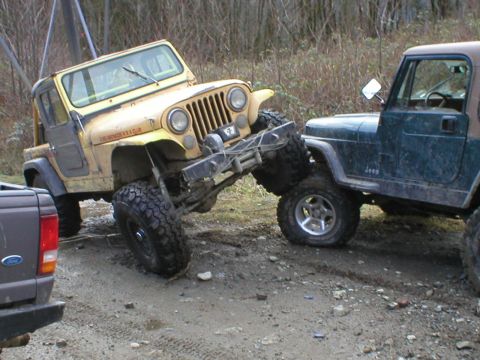 1978 Ford Bronco - Two Jeeps appear to be stuck in a muddy, wooded area, with one vehicle on top of the other.