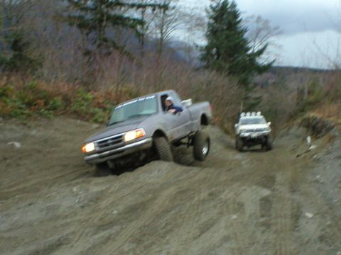 1978 Ford Bronco - Two trucks navigate a challenging dirt terrain on an overcast day.