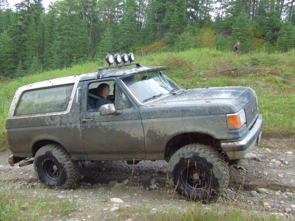 Mud-caked lifted green Ford Bronco side view on rocky trail with roof light bar