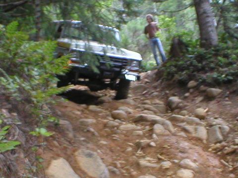 1978 Ford Bronco - A 1978 Ford Bronco tackles a challenging, rocky off-road path with a person standing on the embankment.