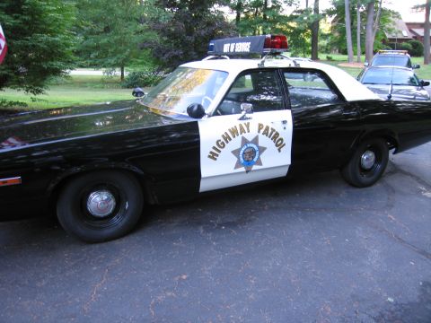 1991 Ford LTD Crown Victoria - black-and-white California Highway Patrol sedan with the CHP star door shield and an Out of Service roof sign, parked on pavement.