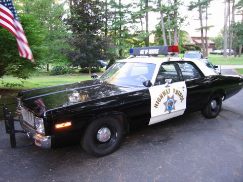 1991 Ford LTD Crown Victoria - Front three-quarter view of a black-and-white California Highway Patrol sedan with push bar and roof lights, beside an American flag.
