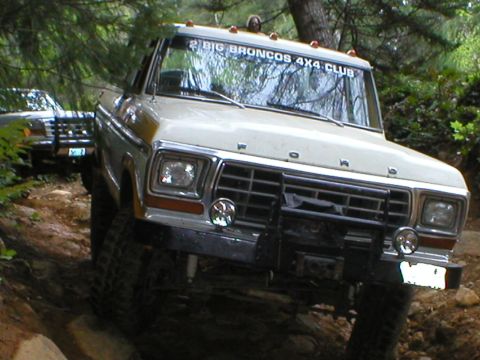 1978 Ford Bronco - Two Ford Broncos navigate a wooded trail, one displaying a club sticker on its windshield.
