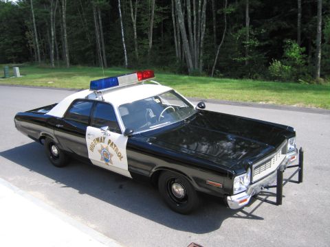 1991 Ford LTD Crown Victoria - High-angle view of a black-and-white HIGHWAY PATROL Dodge sedan with roof lightbar parked on pavement near a grassy treeline.