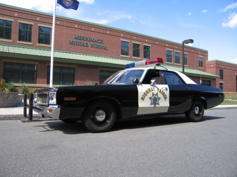 1991 Ford LTD Crown Victoria - Side view of a black-and-white HIGHWAY PATROL Dodge sedan with push bar parked in front of the Merrimack Middle School brick facade.