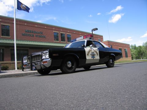 1991 Ford LTD Crown Victoria - Low-angle front three-quarter view of a black-and-white HIGHWAY PATROL Dodge sedan parked in front of Merrimack Middle School.