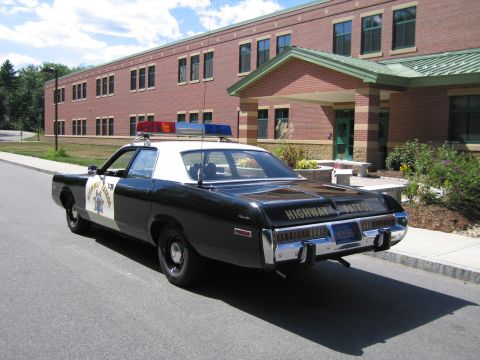 1991 Ford LTD Crown Victoria - Rear three-quarter view of a black-and-white HIGHWAY PATROL Dodge sedan with roof lightbar parked along a curb beside a brick building.