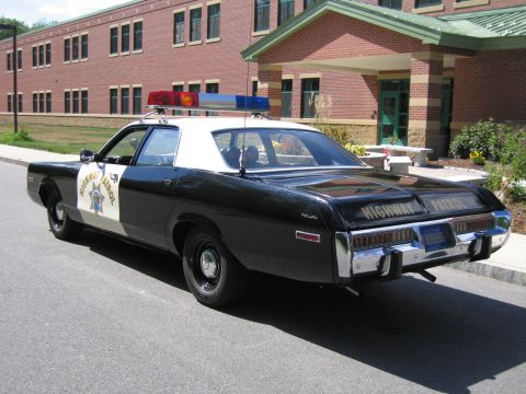 1991 Ford LTD Crown Victoria - Rear three-quarter view of a black-and-white HIGHWAY PATROL Dodge sedan parked at a curb near a brick school entrance and landscaping.