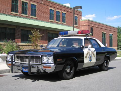 1991 Ford LTD Crown Victoria - Front three-quarter view of a black-and-white HIGHWAY PATROL Dodge sedan with chrome push bar parked beside a long brick building.