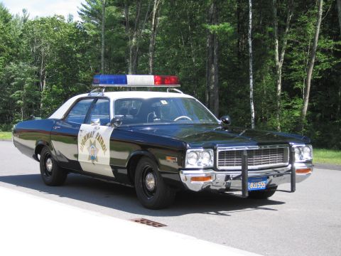 1991 Ford LTD Crown Victoria - Front three-quarter view of a black-and-white HIGHWAY PATROL Dodge sedan with chrome push bar parked on pavement at the edge of the woods.