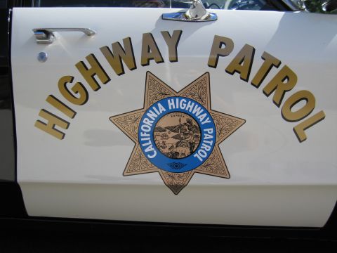 1991 Ford LTD Crown Victoria - Close-up of a white car door showing gold HIGHWAY PATROL lettering and the California Highway Patrol seven-point star badge.