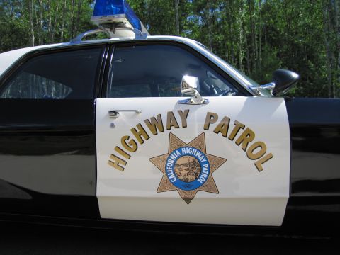 1991 Ford LTD Crown Victoria - Side close-up of a black-and-white CHP car showing the white door with HIGHWAY PATROL lettering, star badge and a blue roof light against a…