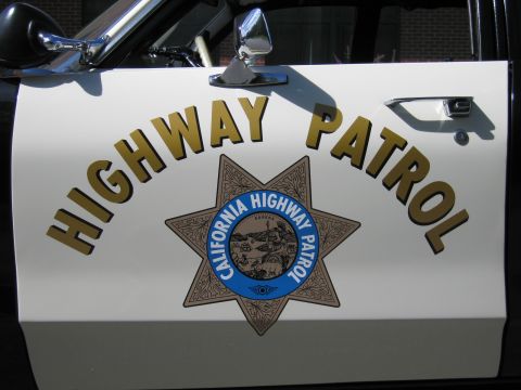 1991 Ford LTD Crown Victoria - Close-up of a white car door showing gold HIGHWAY PATROL lettering and the California Highway Patrol seven-point star badge with chrome sid…