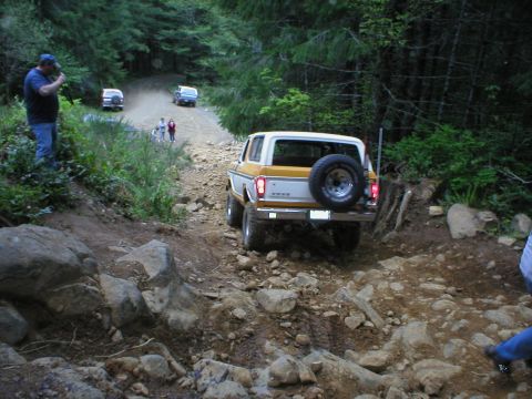 1978 Ford Bronco - A 1978 Ford Bronco navigates a challenging off-road path with other vehicles visible in the distance.