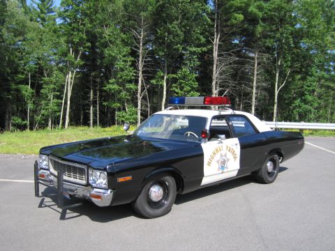 1991 Ford LTD Crown Victoria - Front three-quarter view of a black-and-white HIGHWAY PATROL Dodge sedan with chrome push bar parked in a paved lot beside a wooded area.