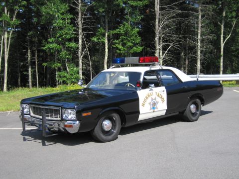 1991 Ford LTD Crown Victoria - black-and-white California Highway Patrol replica cruiser sits on pavement before a wooded backdrop, front three-quarter view.