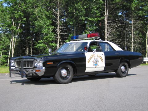 1991 Ford LTD Crown Victoria - black-and-white Highway Patrol police sedan with roof lightbar and push bar, photographed front three-quarter against trees.
