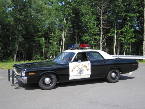 1991 Ford LTD Crown Victoria - black-and-white Highway Patrol sedan with grille guard and lightbar shown in near-profile front view against trees.
