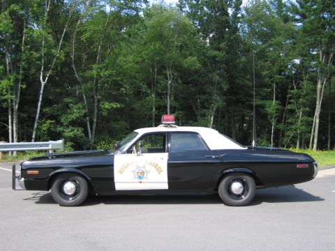 1991 Ford LTD Crown Victoria - black-and-white Highway Patrol police sedan in full side profile with single roof beacon, parked near woods.