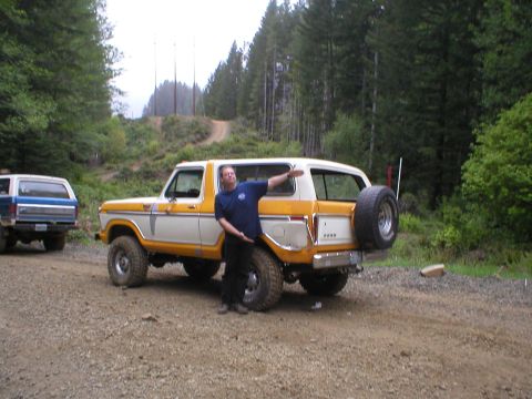 1978 Ford Bronco - A man poses with a white and yellow 1978 Ford Bronco, parked on a dirt road with another SUV in the background.