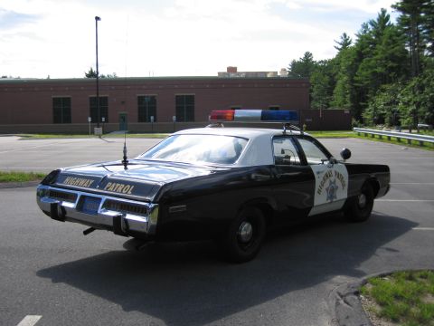 1991 Ford LTD Crown Victoria - black-and-white Highway Patrol sedan with HIGHWAY PATROL lettering on the trunk, rear view in a parking lot by a brick building.