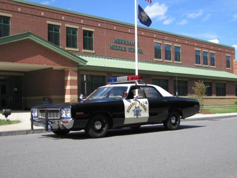 1991 Ford LTD Crown Victoria - black-and-white Highway Patrol cruiser parked before the brick Merrimack Middle School, front three-quarter view.