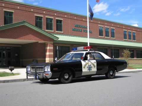 1991 Ford LTD Crown Victoria - black-and-white Highway Patrol cruiser with grille guard parked along a curb before a brick middle school.