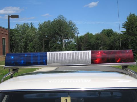 1991 Ford LTD Crown Victoria - Close-up of a police car roof lightbar with blue, white and red sections, mounted above the rear window under a blue sky.