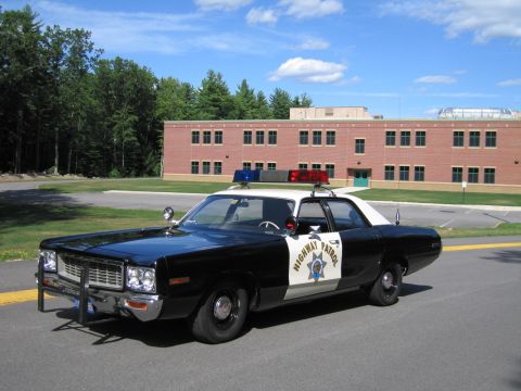 1991 Ford LTD Crown Victoria - black-and-white Highway Patrol police sedan with roof lightbar parked on a road in front of a two-story brick building.