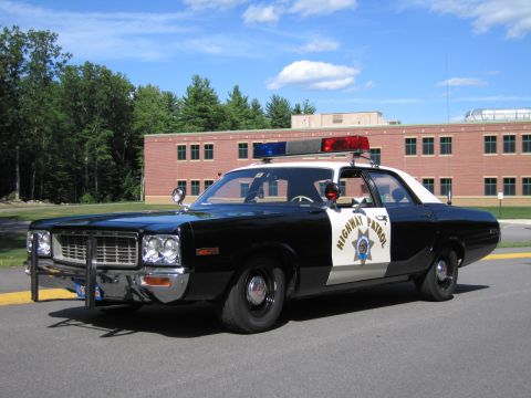 1991 Ford LTD Crown Victoria - Front three-quarter view of a black-and-white Highway Patrol police sedan with grille guard, parked by a brick building.